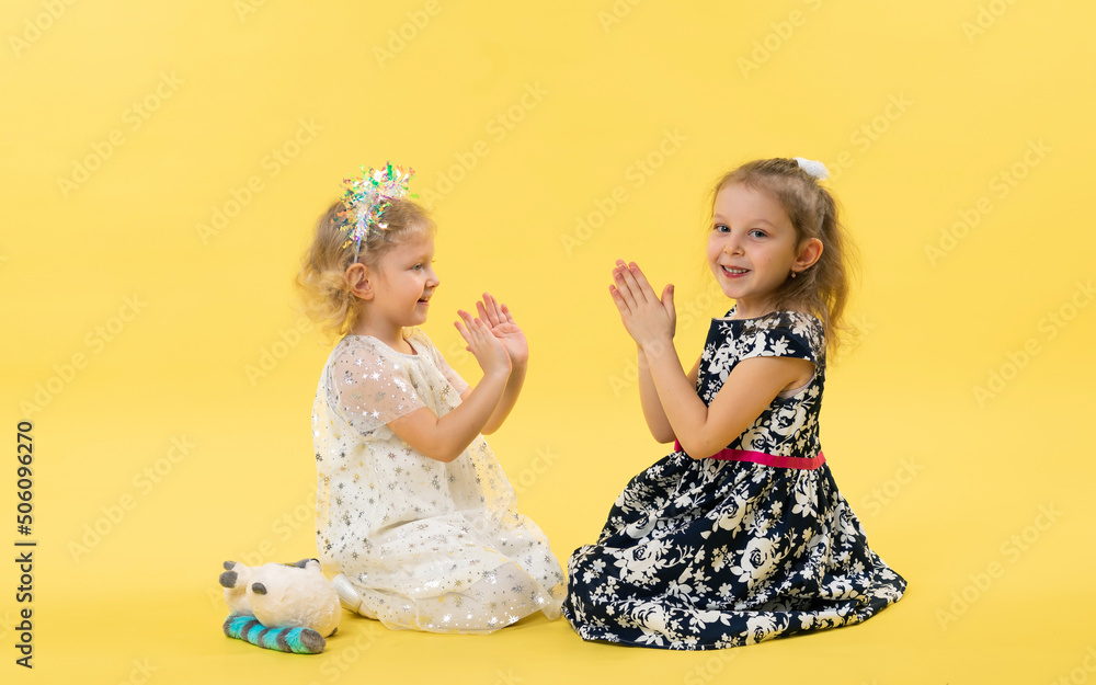Little girls play, sit on the floor in the studio. Yellow background Little girls play, sit on the floor in the studio. Yellow background
