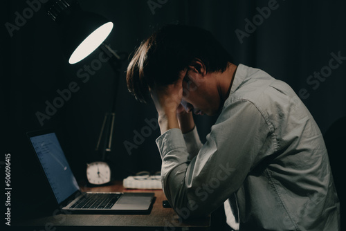 young japanese man holding head due to stress and tiredness at desk