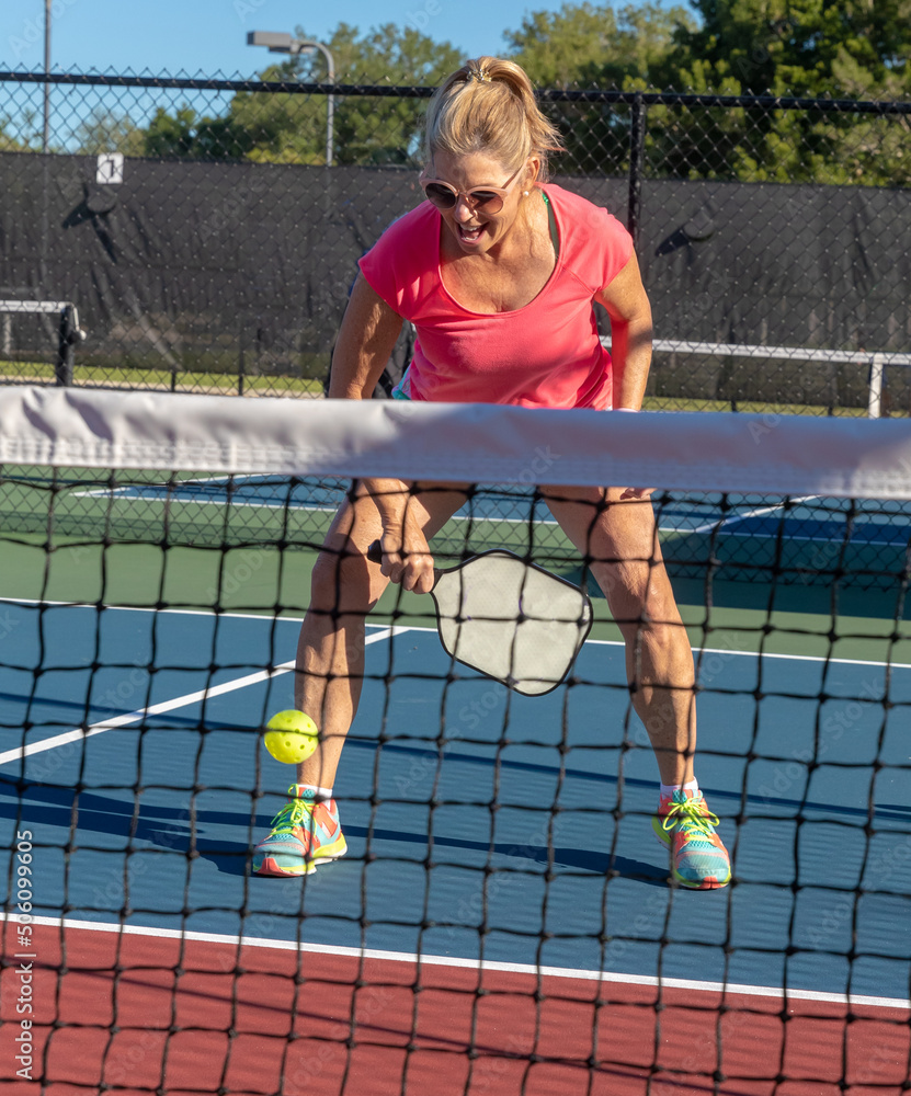 Female Pickleball player attempts to perform a dig shot. Female Pickleball player attempts to perform a dig shot.