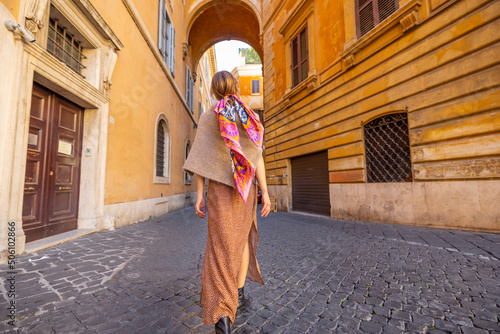 Woman walks on narrow old street with beautiful buildings and arch ahead in Rome. Portrait of a happy stylish woman in Rome. Wide angle view