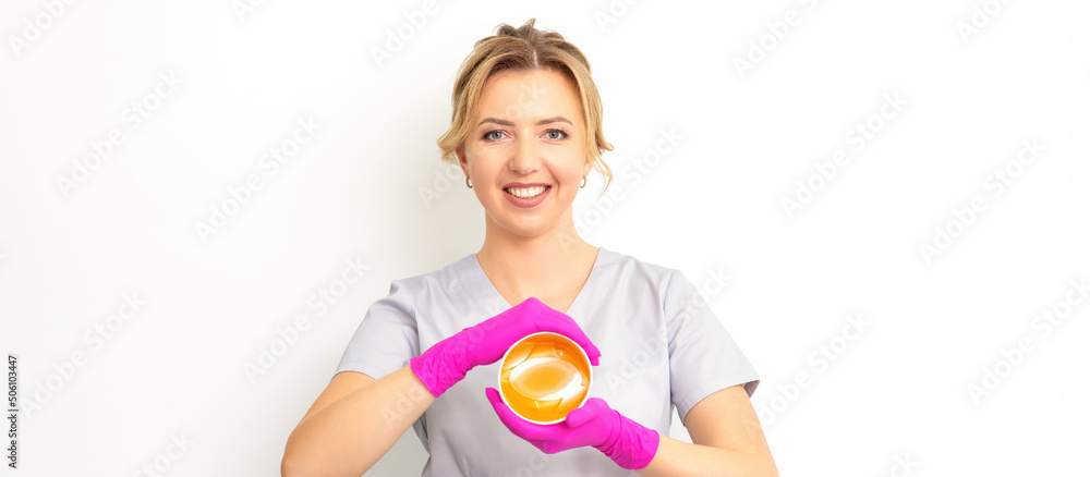 Portrait of a female caucasian beautician holding a jar of sugar paste for sugaring wearing pink gloves on white background Portrait of a female caucasian beautician holding a jar of sugar paste for sugaring wearing pink gloves on white background
