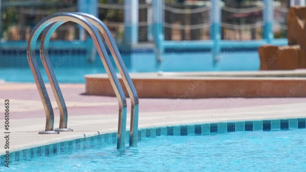 Close up of swimming pool stainless steel handrail descending into tortoise clear pool water. Accessibility of recreational activities concept Close up of swimming pool stainless steel handrail descending into tortoise clear pool water. Accessibility of recreational activities concept