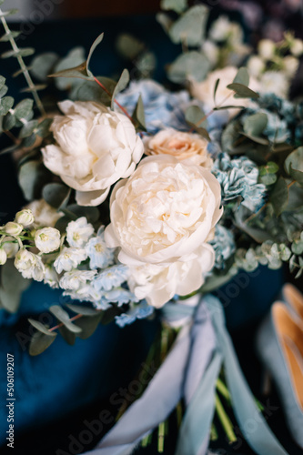 Bridal bouquet. Bridal shoes. Rings. The bride's bouquet. Beautiful bouquet of white, blue, pink flowers and greenery, decorated with long silk ribbon lies on a blue chair