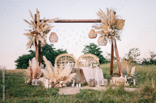 Fabulous wedding for two. Wedding table set up in boho style with pampas grass and greenery, and two straw chair in field with sunset view
