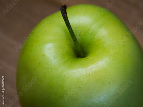 The Reinette Simirenko is an antique apple variety. The fruit has tender, crisp, greenish white flesh with a subacid flavor. A green apple on a wooden tabletop, close-up. photo