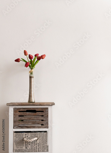 Slim vase with colorful red tulips on vintage wooden table against warm wall on cozy room