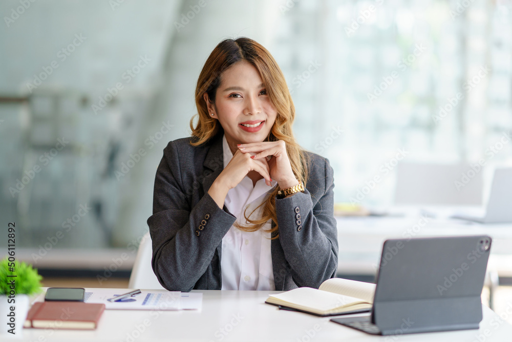 Confident successful Asian business woman sitting smiling looking at camera in office. Confident successful Asian business woman sitting smiling looking at camera in office.