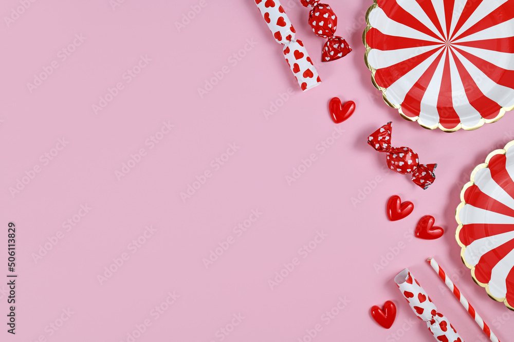 Obraz premium Party flat lay with red paper plates, heart ornaments, candy and drinking straws on pink background with copy space