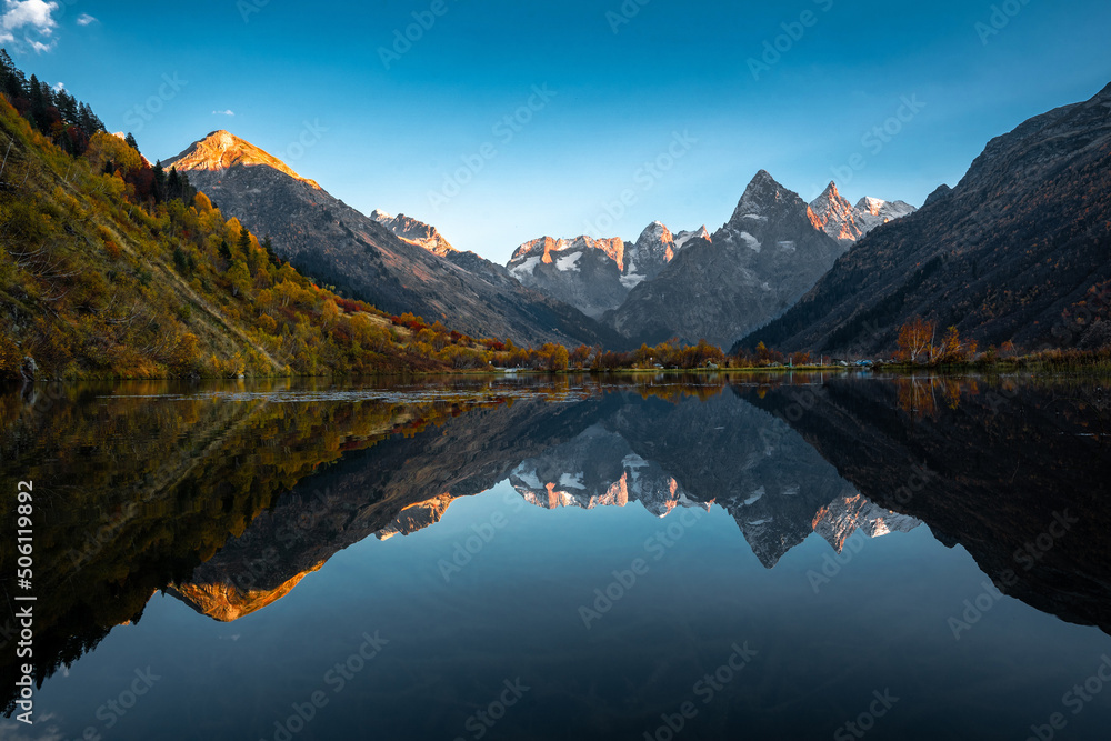 Mountain reflection on the lake. Beautiful landscape with high mountains with illuminated peaks and blue sky. Scenic View Of Lake And Mountains