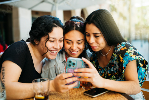 Three young women looking at a phone on terrace of a restaurant