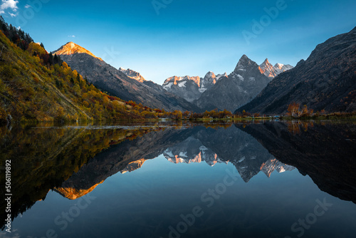 Mountain reflection on the lake. Beautiful landscape with high mountains with illuminated peaks and blue sky. Scenic View Of Lake And Mountains © SDF_QWE