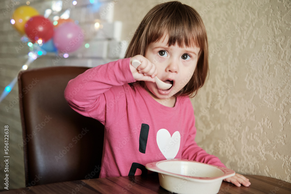 Cute Little Girl 2 Years alone eats porridge with a spoon.
