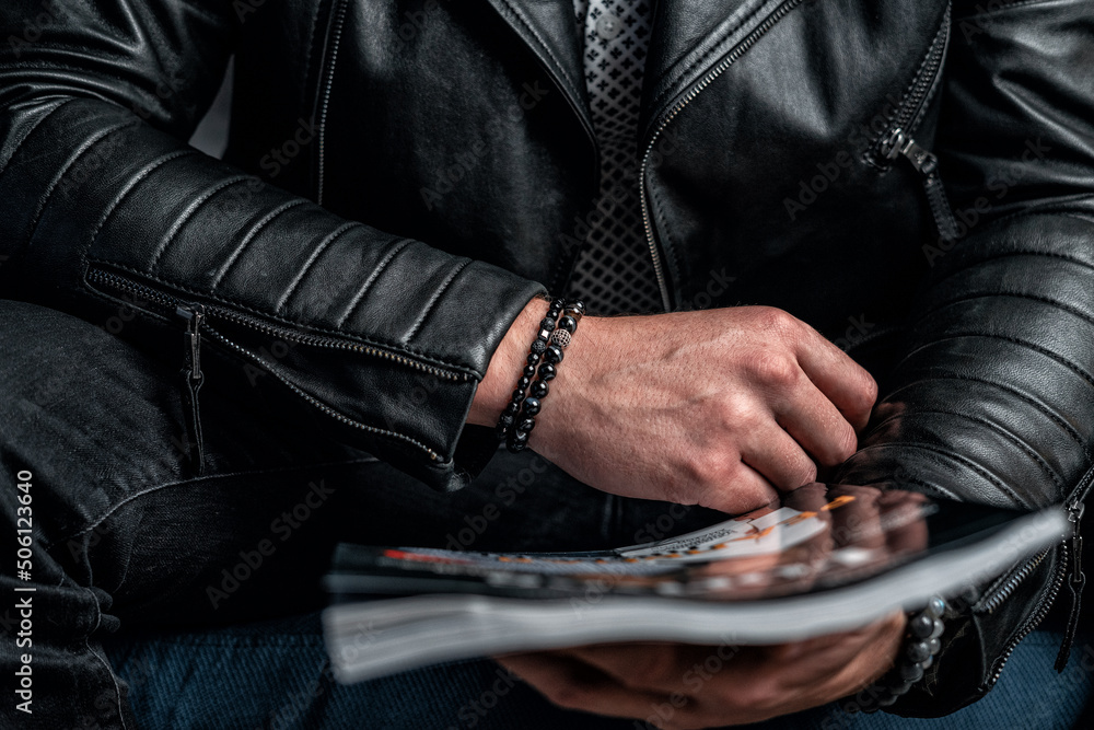 Fototapeta premium A black bracelet made of expensive stones on a man's hand, a leather jacket and a magazine