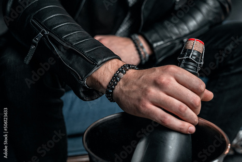 Two stylish men's bracelets, on the wrist. Champagne bottle in hand, black background photo
