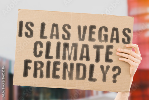 The question " Is Las Vegas climate-friendly? " is on a banner in men's hands with blurred background. Support. Team. Activist. Urban. Sunset. Carbon. Ecology. Energy. New. Clean. Warming. Waste