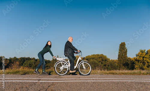 Young smiling caucasian girl on roller skates and a man on a electric bike fun ride together. Active leisure and hobbies. Father and daughter.