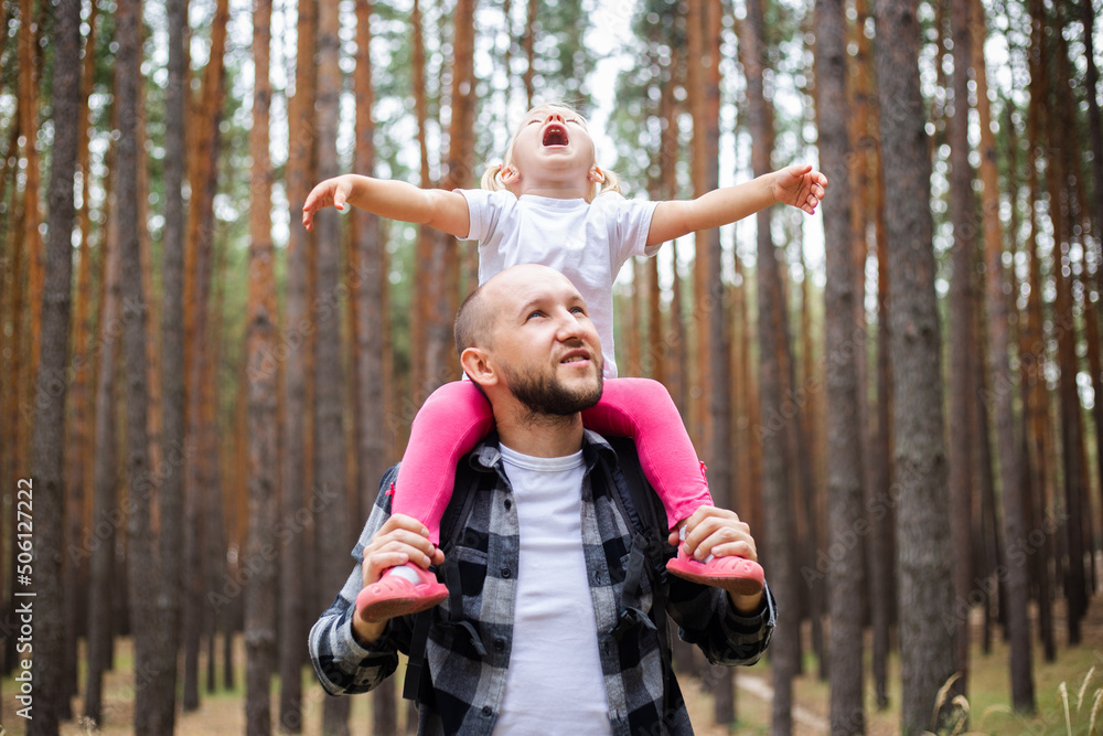 Man with a backpack carries a child on his shoulders in the forest. Family hike to the mountains or forest Man with a backpack carries a child on his shoulders in the forest. Family hike to the mountains or forest