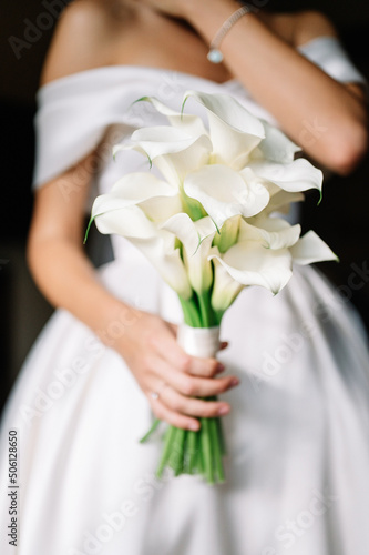 Beautiful wedding bouquet of white callas in hands of a young bride with a beautiful wedding manicure on nails.