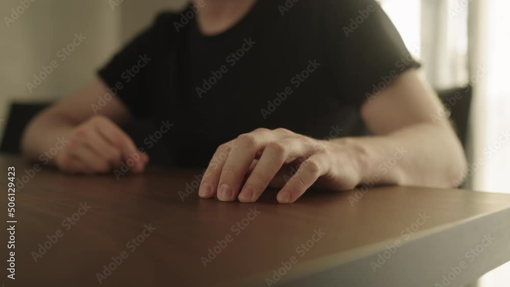 Man sitting in a chair and finger tapping on a walnut table with bright sunlight from a window behind Man sitting in a chair and finger tapping on a walnut table with bright sunlight from a window behind