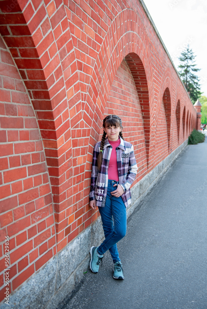 A teenage girl stands near a brick wall. Beautiful brick wall