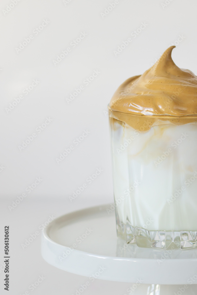 Close-up of Dalgona coffee with creamy texture on top, served in a clear glass on a white stand. Close-up of Dalgona coffee with creamy texture on top, served in a clear glass on a white stand.