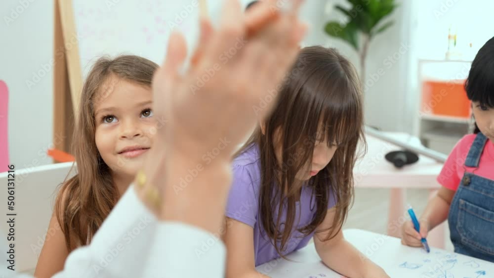 Woman teacher teaching little girl to paint color book on the table in classroom,kindergarten education school.Multi-ethnic preschool teacher and students in classroom.Kindergarten and study concept. Woman teacher teaching little girl to paint color book on the table in classroom,kindergarten education school.Multi-ethnic preschool teacher and students in classroom.Kindergarten and study concept.