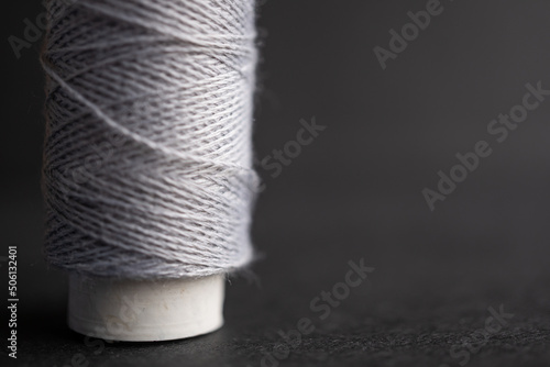 detalle de un carrete de hilo de algodón color gris sobre fondo obscuro