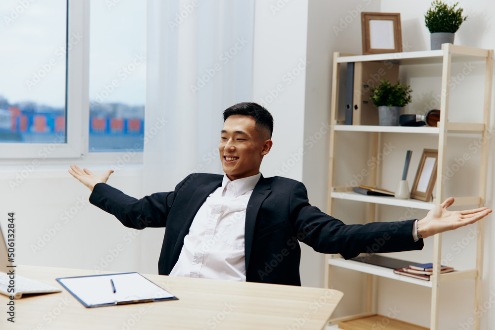 Asian man in a suit sits at a table in front of a computer technologies