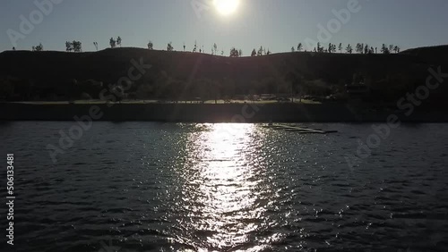 aerial footage of the sun reflecting off a rippling lake at sunset with rocks and lush green trees and grass on the banks of the lake at Castaic Lake in Castaic California USA photo