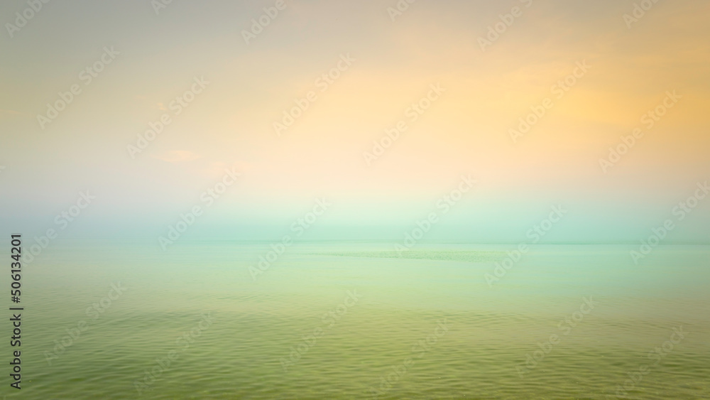 Sunrise seascape with warm pastel-toned sky, horizon, and waves in the Atlantic Ocean on a foggy morning