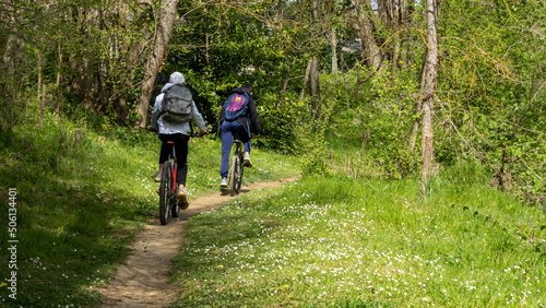 Young teenagers cycling on a grassy path, from behind, in the spring