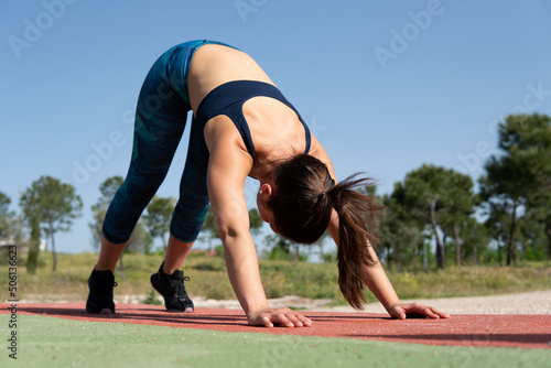 Young woman stretching shoulders before training. Athlete brunette girl leaning on the floor of the calisthenics park to warm up her muscles to perform hard acrobatic exercises with her body weight.