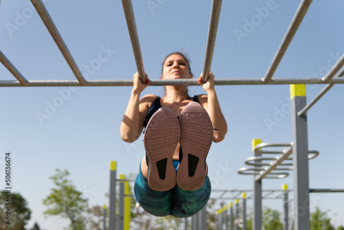 Sporty woman doing a neutral pull-up on the calisthenics bars. Young brunette girl raising her body with her arms holding a fixed bar with her hands for sports. photo