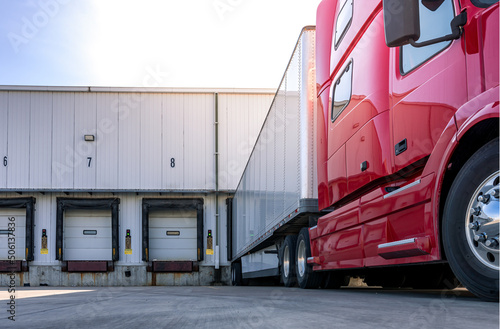 Fotografia, Obraz Red modern American semi truck parked at the docks, waiting to get loaded