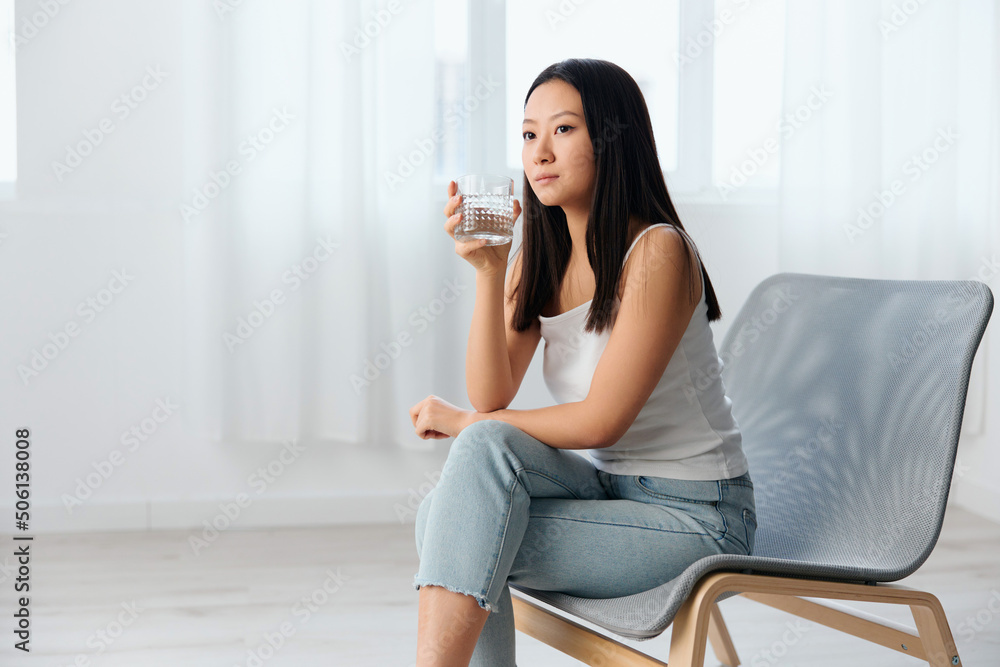 Pensive dreaming young Asian cute woman think about bad relationships hold glass of water sit on chair in light office interior. Breakup from work. Relaxing time concept. Copy space Offer Pensive dreaming young Asian cute woman think about bad relationships hold glass of water sit on chair in light office interior. Breakup from work. Relaxing time concept. Copy space Offer