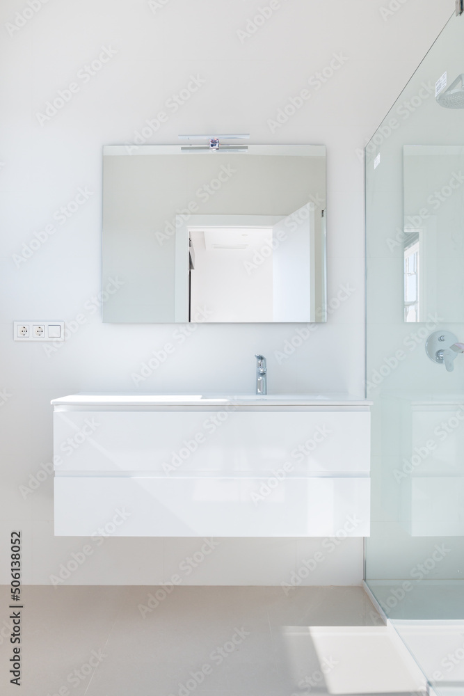 Part of a modern bathroom. A view of a white cabinet with a sink and a glass shower cubicle. Part of a modern bathroom. A view of a white cabinet with a sink and a glass shower cubicle.