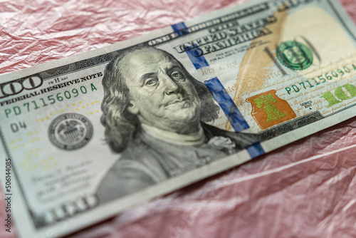 textured background of one hundred dollar bill with a portrait of us President Franklin in orange, red and black colors. blur, defocus.