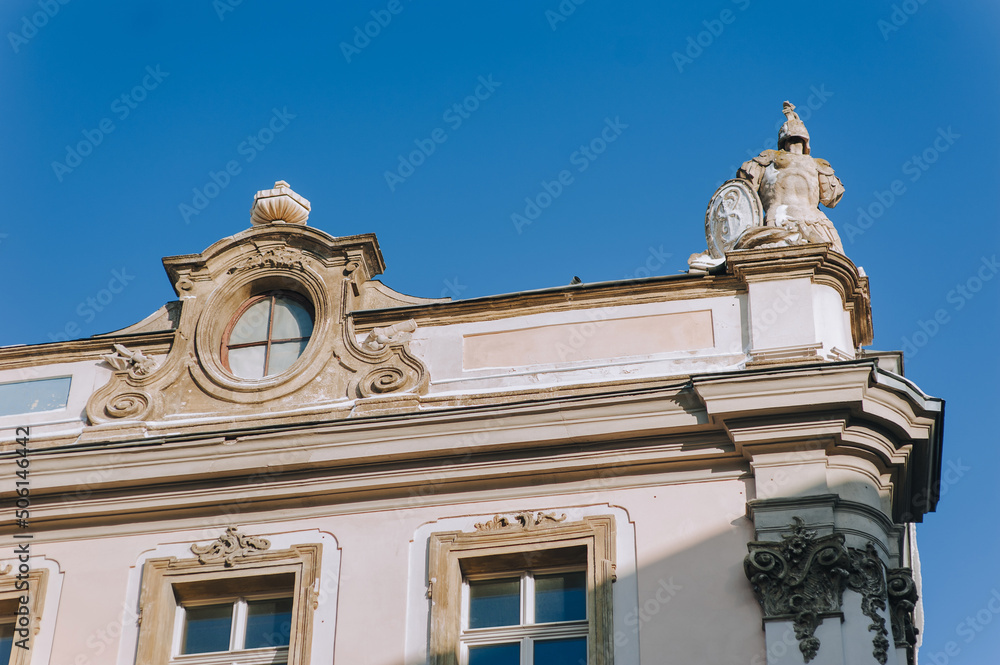Lubomirski Palace in Lviv, Ukraine. The facade of the old baroque house with an oval window and sculptures on the roof in the form of military knightly armor on blue sky background.