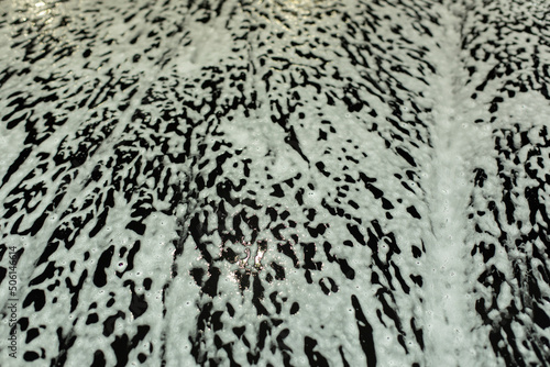 Soap foam on car. Texture of white foam on black car. Washing of transport.
