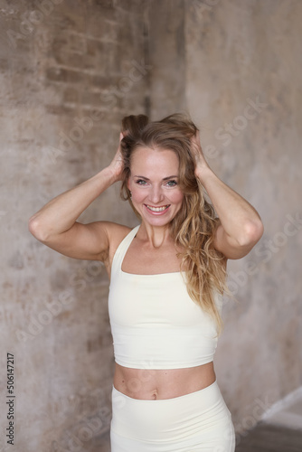 Portrait of 30-year-old sports woman. beautiful strong muscular woman posing in gym. Healthy young adult woman in light sportswear stretch alone. Fit thin gimnast smiling and flirting © Tatyana