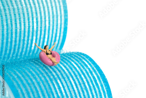 Miniature people toy figure photography. Girl wearing black sunglass riding rubber tube ring playing pipeline tunnel in water park, pool water sport activity. photo