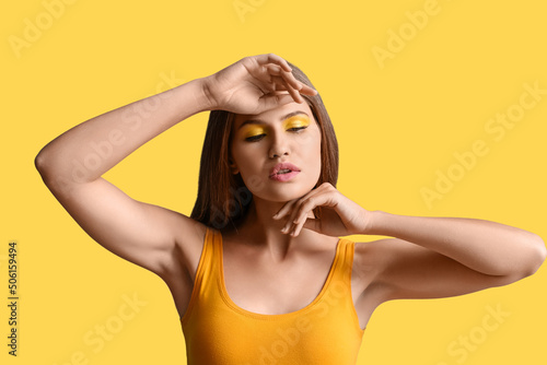 Beautiful young woman with bright makeup on yellow background