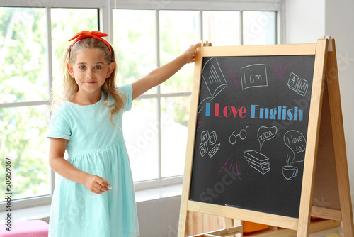 Cute little girl near chalkboard with text I LOVE ENGLISH