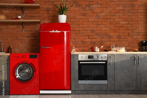 Interior of modern kitchen with red washing machine and fridge near brick wall