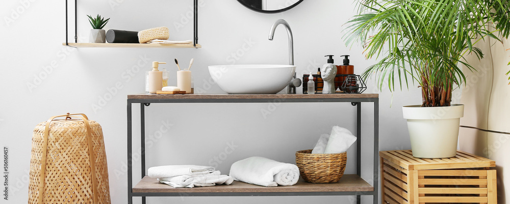 Table with different bath accessories and modern sink near light wall Table with different bath accessories and modern sink near light wall