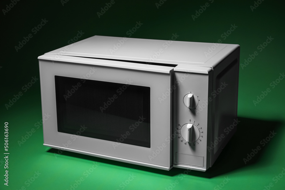 Fototapeta premium White microwave oven with opened door on green background
