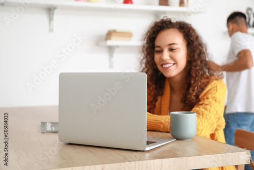 Young African-American woman using laptop at table in kitchen, closeup