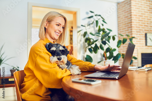 Smiling middle aged woman holding dog using laptop while at home office © baranq