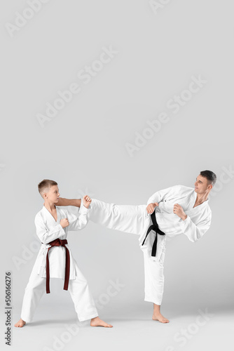 Boy practicing karate with instructor on light background