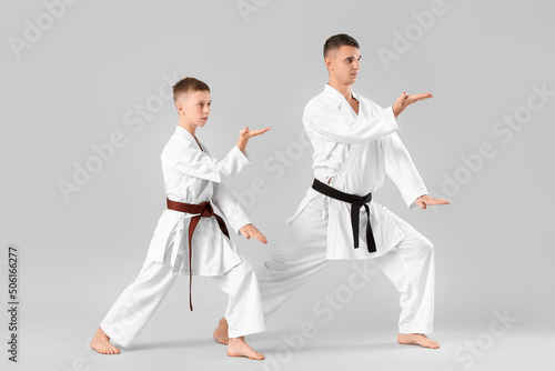 Boy practicing karate with instructor on light background